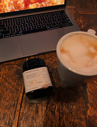 Laptop, bottle of Manuka Honey, and cup of coffee on a wooden table.